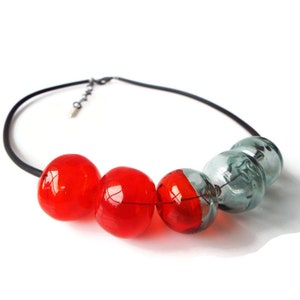 May include: A necklace with a black cord and five glass beads. Three of the beads are red and two are a light gray color.
