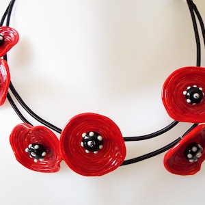 May include: A red and black necklace with multiple red poppy flower charms. The necklace is made of black elastic cord and the poppy flowers are made of paper.