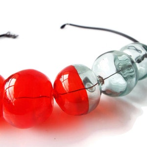 May include: A necklace made of red and clear glass beads. The beads are strung on a black wire.