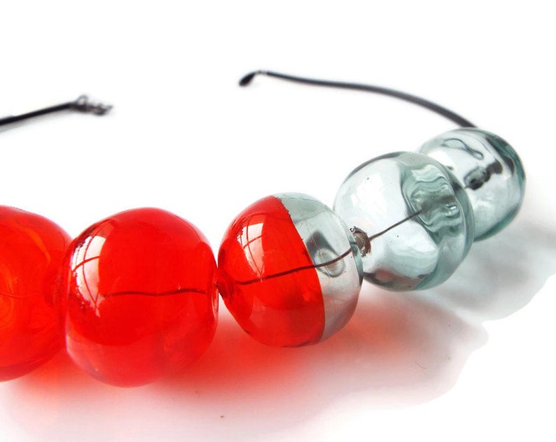 May include: A necklace made of red and clear glass beads. The beads are strung on a black wire.