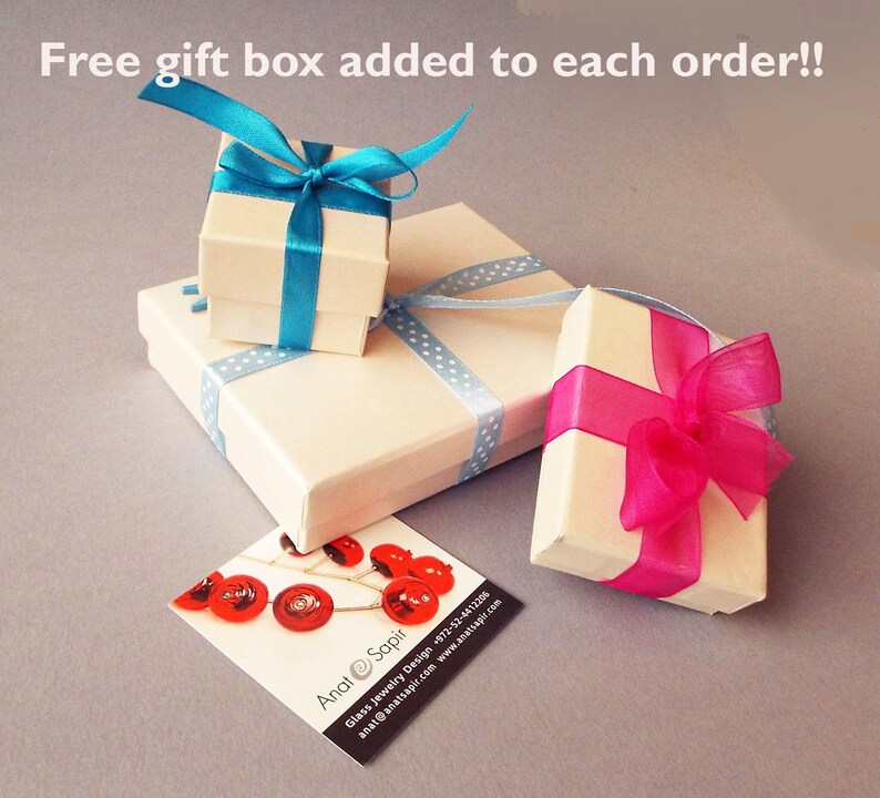 May include: Two white gift boxes with blue and pink ribbon bows. The boxes are on a light gray surface. The text "Free gift box added to each order!!" is at the top of the image. The text "Anat Sapir" is on a business card in the lower right corner of the image.