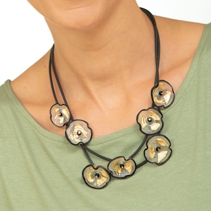 May include: A black necklace with gold accents features a series of round, clear glass pendants with gold leaf designs. The necklace is layered and has a simple, modern aesthetic.