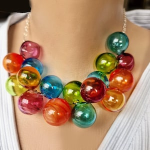 May include: A colorful necklace featuring large, round, transparent beads in shades of red, orange, yellow, green, blue, and purple. The beads are strung on a silver chain, creating a vibrant and eye-catching accessory.