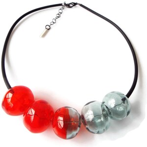 May include: A black choker necklace with red and gray glass beads. The beads are round and have a slightly irregular shape.