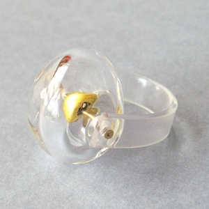 Peut inclure: Une bague en plastique transparent avec un accent doré sur le dessus. La bague est conçue pour ressembler à une cloche.