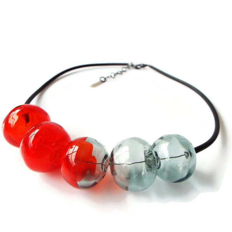 May include: A necklace with a black cord and large, round glass beads. The beads are a gradient of red and gray.