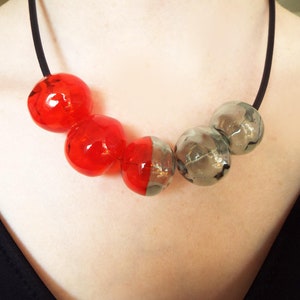 May include: A necklace with alternating red and gray glass beads. The beads are round and have a slightly textured surface.