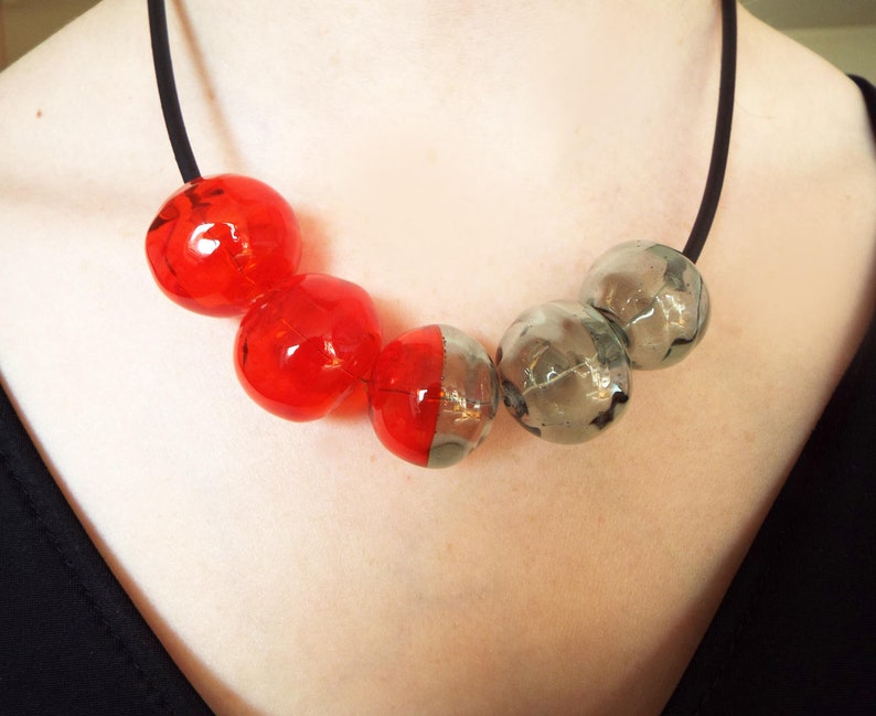 May include: A necklace with alternating red and gray glass beads. The beads are round and have a slightly textured surface.