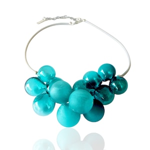 May include: A turquoise blue glass bead necklace with a silver chain. The beads are clustered together in a cascading design.
