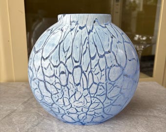 May include: A round, light blue vase with a textured, crackle-like pattern in darker blue. The vase has a wide, spherical body and a slightly narrower opening at the top. The design gives the vase a unique, artistic appearance.
