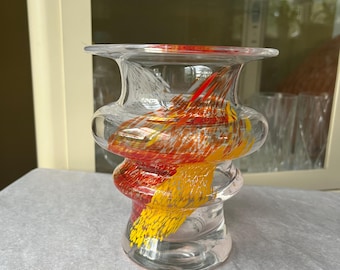 May include: Clear glass vase with a unique, twisted design. The interior features vibrant streaks of red, yellow, and orange, creating a colorful, abstract pattern. The vase has a wide top and base, with a narrower, spiraled midsection.
