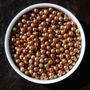 May include: A bowl filled with a large quantity of small, round, iridescent pearls in shades of brown and gold.