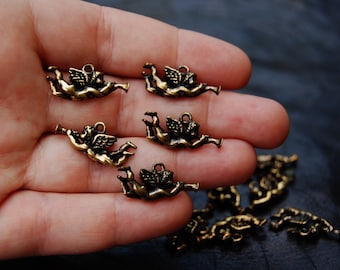 May include: A close-up of a hand holding several small, gold-colored angel charms. The angels are depicted with wings and are playing trumpets.