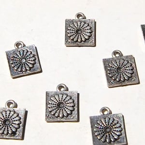 May include: Ten silver-toned metal charms with a square shape and a raised floral design. Each charm has a loop at the top for attaching to a necklace, bracelet, or other jewelry.