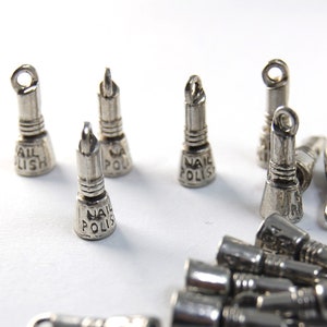 May include: Silver-toned metal charms shaped like nail polish bottles. Each charm has the words "Nail Polish" engraved on the side.