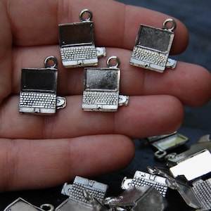 May include: A close-up of a hand holding five silver laptop charms. The charms are detailed with a screen, keyboard, and a small opening for a CD drive. The charms are arranged in a row on the hand, with the top charm slightly offset from the others.