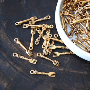 May include: A collection of gold-toned metal fork charms with a rose detail. The charms are scattered on a dark brown wooden surface.
