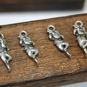 May include: Four silver charms depicting a figure playing a musical instrument. The charms are on a wooden surface.