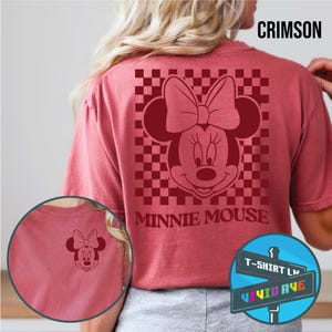 May include: A red t-shirt with a checkered pattern and a red Minnie Mouse graphic. The text "Minnie Mouse" is printed below the graphic. The shirt is available in a crimson color.