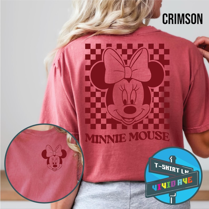 May include: A red t-shirt with a checkered pattern and a red Minnie Mouse graphic. The text "Minnie Mouse" is printed below the graphic. The shirt is available in a crimson color.