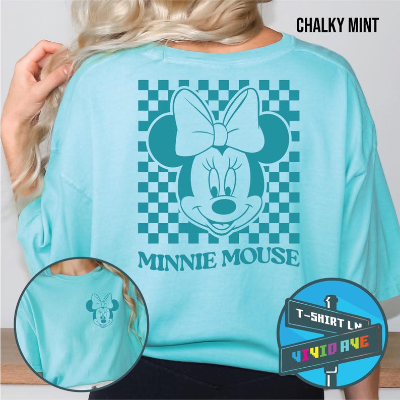 May include: A light blue t-shirt with a checkered background and a cartoon image of Minnie Mouse. The text "Minnie Mouse" is printed below the image. The t-shirt is available in size large.