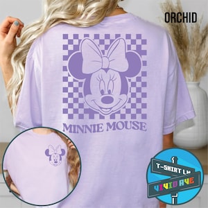 May include: A purple t-shirt with a checkered pattern and a purple Minnie Mouse graphic. The text "Minnie Mouse" is printed below the graphic. The shirt is available in the color "Orchid".