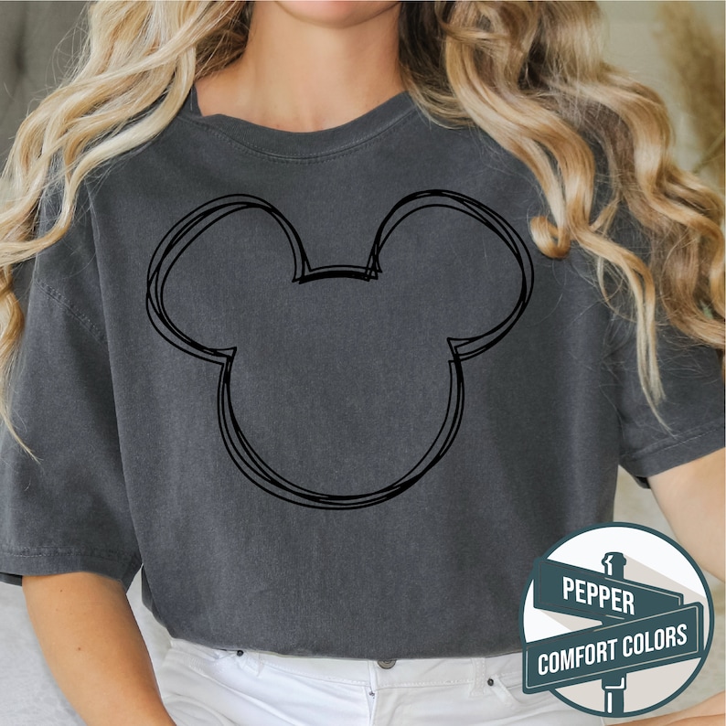 Puede incluir: Camiseta gris oscuro con un contorno negro de la cabeza de Mickey Mouse. La camiseta tiene cuello redondo y mangas cortas. El texto en el letrero dice "Pepper Comfort Colors".