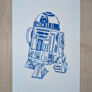 Könnte beinhalten: Ein blauer und weißer Linienkunst-Druck von R2-D2, einem Robotercharakter aus dem Star Wars-Franchise.