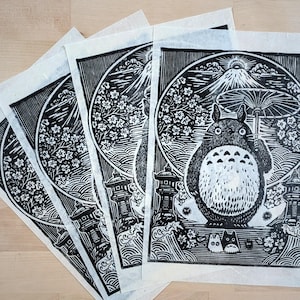 May include: A collection of black and white art prints featuring a whimsical illustration of a Totoro-like creature holding an umbrella. The prints showcase a mountain, cherry blossoms, and traditional Japanese elements.