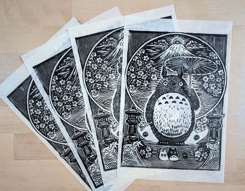 May include: A collection of black and white art prints featuring a whimsical illustration of a Totoro-like creature holding an umbrella. The prints showcase a mountain, cherry blossoms, and traditional Japanese elements.