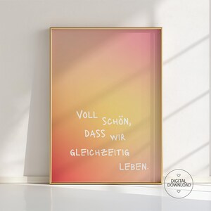 May include: A framed print with a gradient background of orange, yellow, and pink hues. The text "Voll Schön, dass wir gleichzeitig leben" is written in white script. A digital download icon is in the bottom right corner.