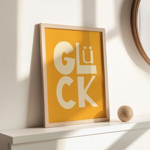 Gelbes Typografie Poster mit dem Wort „Glück“. Modernes glücklich Wandbild für Wohnzimmer, Küche oder Büro. Strahlt Motivation, Energie und Positivität aus – perfekt als Geschenk oder Deko für Zuhause und Familie.