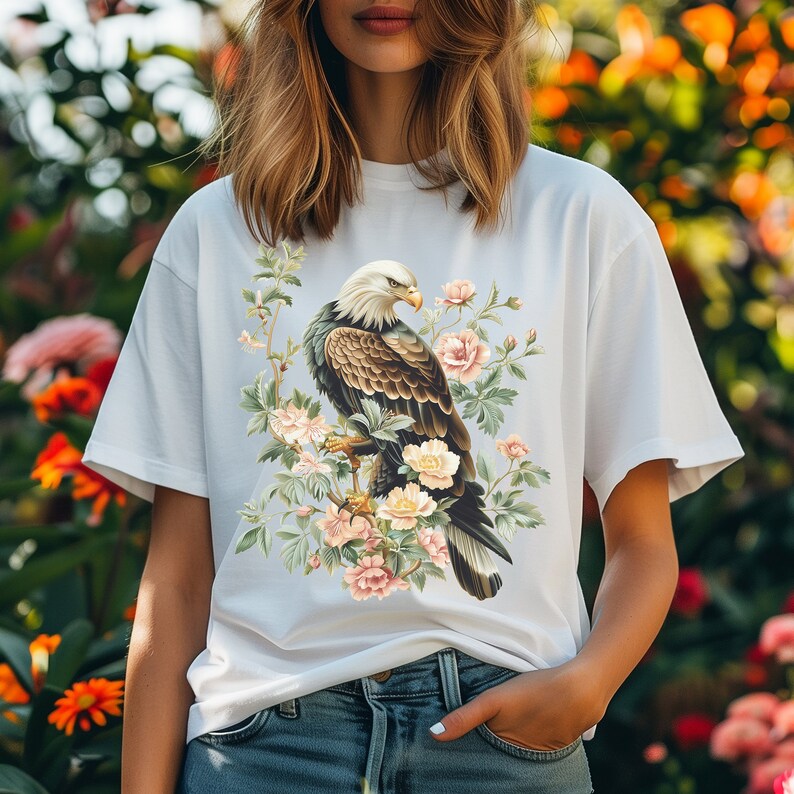 May include: White t-shirt with a graphic print of a bald eagle perched on a branch with pink flowers.