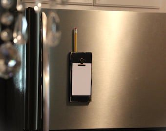 May include: A black wooden clipboard with a gold clip is attached to a stainless steel refrigerator. A yellow pencil is attached to the clipboard with a red eraser.