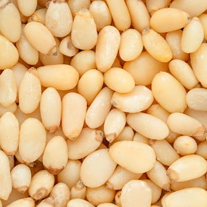 May include: Close-up shot of a pile of raw pine nuts. The nuts are oval-shaped, with a creamy beige color and a slightly translucent appearance. The texture appears smooth and slightly oily.