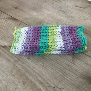 Könnte beinhalten: Ein gefalteter Strick-Geschirrtuch in den Farben Lila, Grün und Weiß. Das Geschirrtuch ist mit einem einfachen Strickmuster gearbeitet und hat ein gestreiftes Muster.