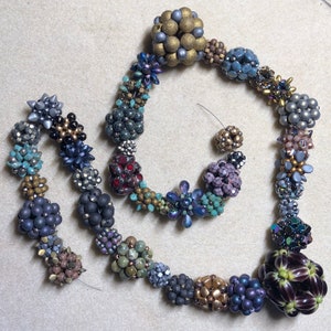 May include: A multi-colored beaded necklace with a variety of shapes and sizes. The necklace is made of glass beads, metal beads, and other materials. The beads are arranged in a pattern that is both intricate and eye-catching.