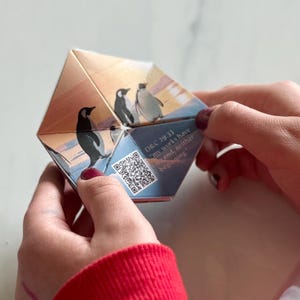 Könnte beinhalten: Ein gefaltetes Papierpinguin-Bastelwerk mit einem QR-Code und dem Text "Dec. 29-31  Tom & Mia Have  a Small Birthday  Gathering".