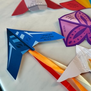 May include: A selection of colourful paper crafts, including a blue paper aeroplane with orange and red ribbons, a purple butterfly, and other geometric shapes. Each piece has text that reads "I will give you a pattern in all things D&C 52:14."