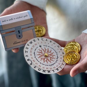 May include: A white cardboard treasure chest with the text "Seek to walk in wisdom's paths" and "Proverbs 12:15-21". A white cardboard compass with a gold star and the text "surely the Lord God will meet us" and "Proverbs 3:5-7". Four gold-coloured coins with a compass design.