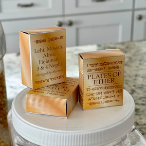 May include: Three small boxes with gold and white text. The boxes are labeled "Lehi, Mosiah, Alma, Helaman, 3 & 4 Nephi Abridged by Mormon", "Plates of Ether", and "MOR PLATES".