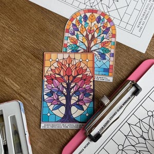 Puede incluir: Dos impresiones artísticas de vidrieras de colores con un diseño de árbol en varios colores. También se ven un clip plateado y una paleta de acuarelas. Las impresiones tienen el texto "Buscad diligentemente, orad siempre, y todas las cosas cooperan para bien."