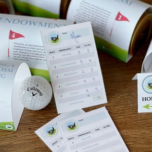 Może przedstawiać: Plansza do gry w golfa z białą piłką golfową i kartami punktowymi. Karty punktowe są oznaczone nazwami obrzędów LDS, takich jak chrzest, konfirmacja, kapłaństwo, endowment i pieczętowanie. Plansza do gry jest ozdobiona zieloną trawą i białą flagą.