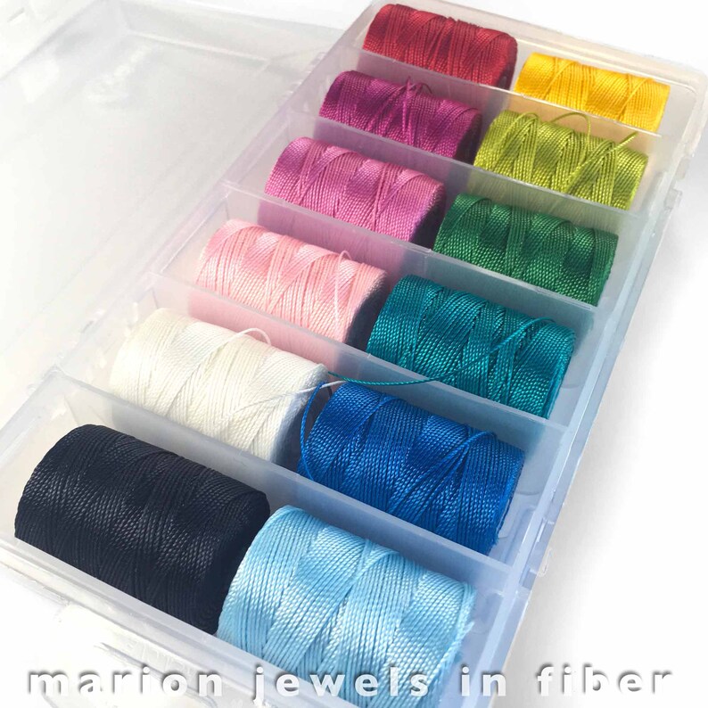 May include: A clear plastic storage box with 10 spools of colorful thread. The spools are arranged in a rainbow pattern, starting with red and ending with light blue.