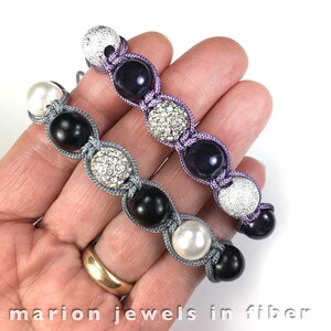 May include: Two bracelets with knotted cord and various beads. One bracelet has black, white, and gray beads. The other bracelet has purple, silver, and clear beads.