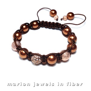 May include: A brown cord bracelet with brown and gold beads. The bracelet has a sparkly gold bead and a textured gold bead.