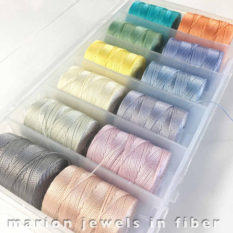 May include: A clear plastic storage box filled with spools of colorful thread. The thread colors are a gradient from teal to peach.