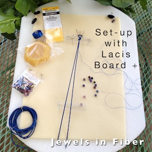 Puede incluir: Primer plano de una tabla de espuma blanca con hilo azul, cuentas y agujas. El texto "Set-up with Lacis Board + Jewels in Fiber" está impreso en la tabla.