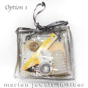 May include: A clear plastic bag with a drawstring closure, containing various craft supplies, including a yellow ruler, a white measuring tool, and a spool of thread. The bag is labeled "marion jewels in fiber".