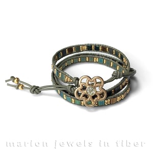 Könnte beinhalten: Ein grünes Lederarmband mit einem goldenen Blumenanhänger und blauen und goldenen Perlen. Das Armband ist von Marion Jewels in Fiber.